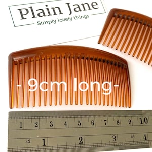 May include: Two brown plastic combs, one is 9 centimeters long. The combs are on a white surface with a ruler.