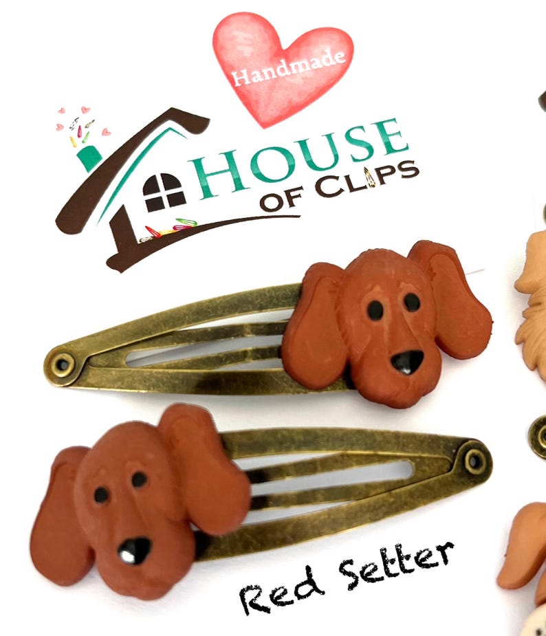May include: Two red setter dog hair clips with bronze-colored metal clasps. The clips feature a 3D dog head design. The image also includes the text "House of Clips" and "Red Setter".