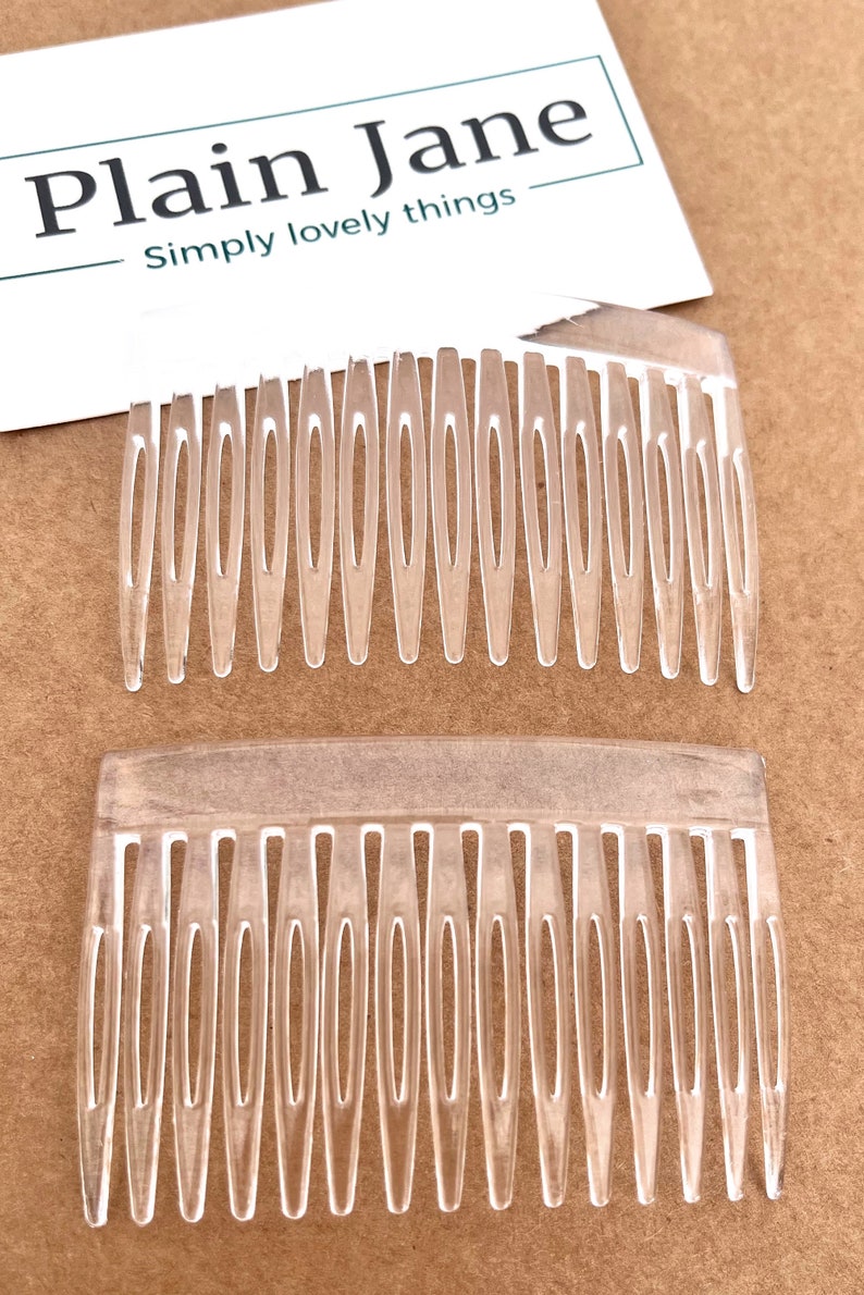 May include: Two transparent plastic hair combs with multiple teeth. The combs are on a brown surface. A white card with the text "Plain Jane" and "Simply lovely things" is in the background.