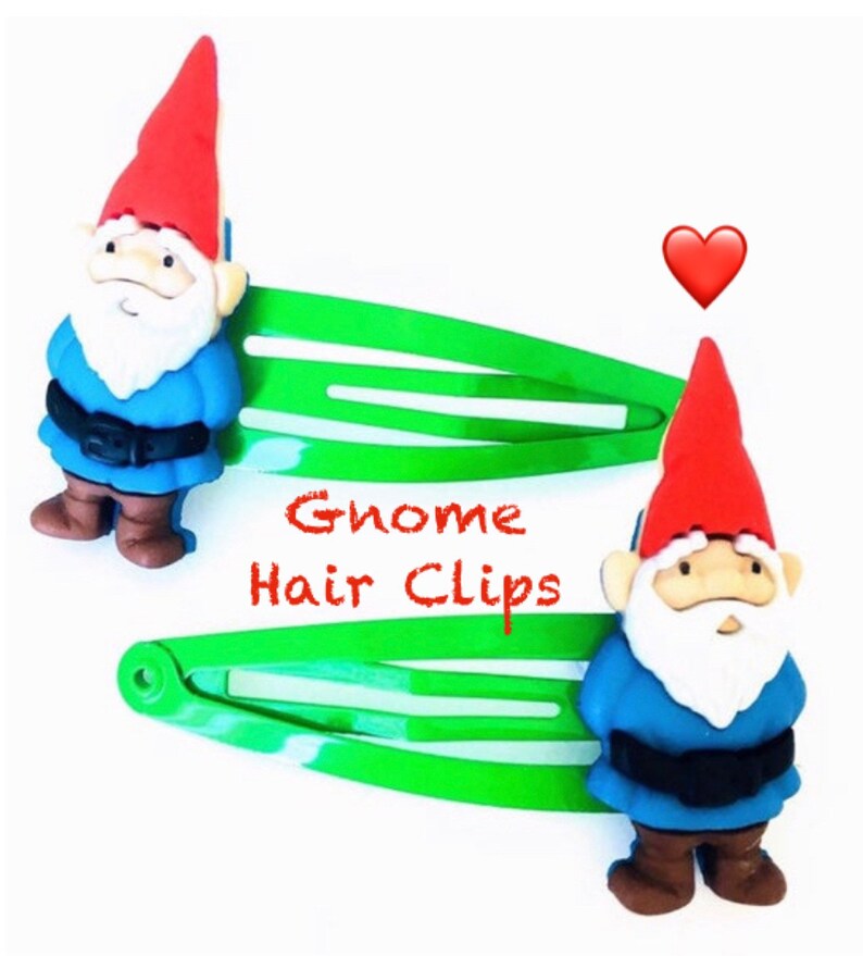 May include: Two green alligator hair clips with a gnome charm on each. The gnomes are wearing blue shirts, brown pants, and red hats. The text "Gnome Hair Clips" is written in red letters on the clips.