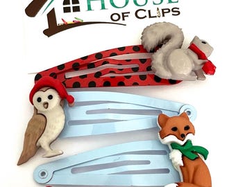 May include: Set of four colorful hair clips featuring animal designs. The clips are decorated with a squirrel, owl, fox, and bird wearing Santa hats. The clips are handmade by House of Clips.