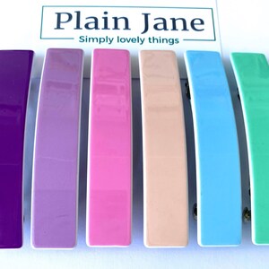 May include: Set of six colorful hair clips. The clips are made of plastic and have a glossy finish. The colors are purple, lavender, pink, peach, light blue, and mint green.