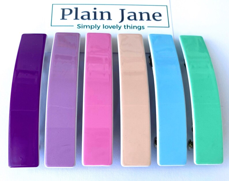May include: Set of six colorful hair clips. The clips are made of plastic and have a glossy finish. The colors are purple, lavender, pink, peach, light blue, and mint green.