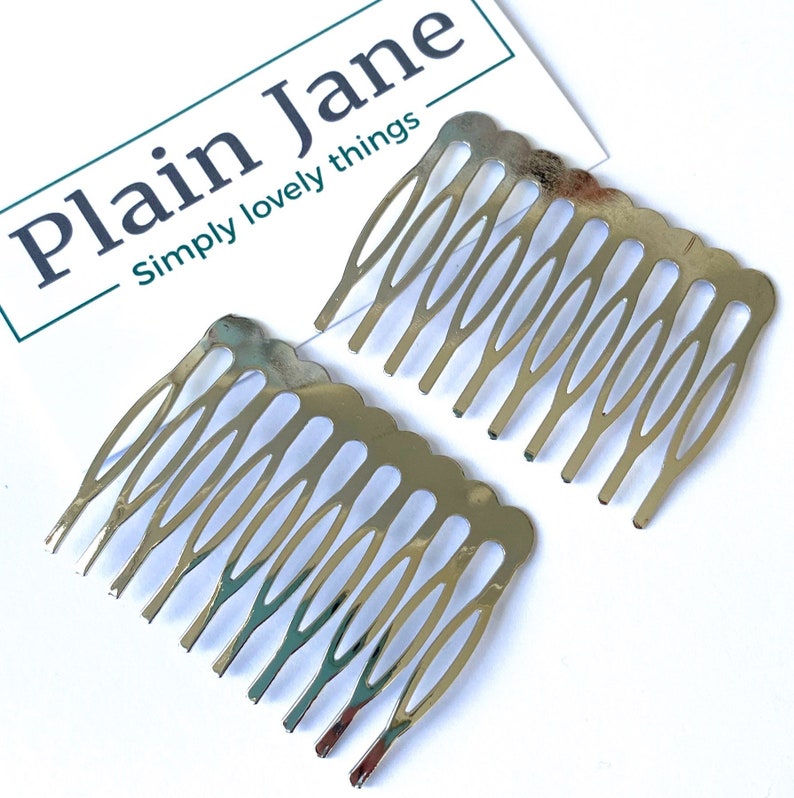 May include: Two silver hair combs with a decorative design. The combs are made of metal and have a shiny finish.