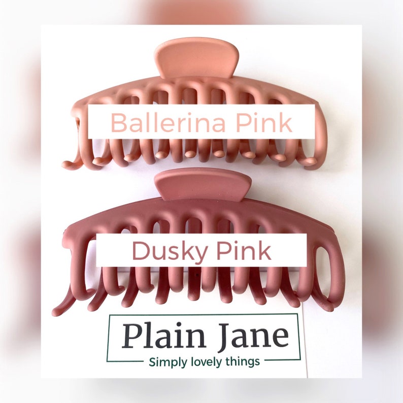 Puede incluir: Dos grandes pinzas para el pelo de pl&aacute;stico en tonos rosados. La pinza superior es de un tono rosa m&aacute;s claro y est&aacute; etiquetada como "Ballerina Pink". La pinza inferior es de un tono rosa m&aacute;s oscuro y est&aacute; etiquetada como "Dusky Pink". El texto "Plain Jane" est&aacute; debajo de las pinzas con el lema "Simply lovely things".
