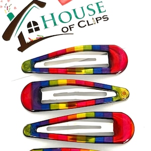 May include: Set of four rainbow-colored plastic hair clips. The clips are in the shape of an oval and have a metal spring. The clips are arranged in a row, with the largest clip at the top and the smallest clip at the bottom. The clips are all decorated with a rainbow stripe pattern.