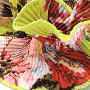 May include: Close-up of a pleated fabric with a floral print in shades of pink, red, white, and brown. The fabric has a lime green trim around the edges.