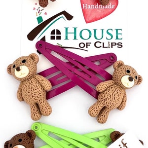 May include: Set of four brown teddy bear hair clips with yellow, green, and purple plastic barrettes. The clips are handmade and come with a note that says "Message me if you'd like a different clip colour".