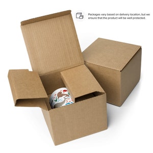 May include: A brown cardboard box with a white mug inside. The mug has a colorful design of animals and plants. The box is open and the mug is visible. The box is sitting on a white surface.