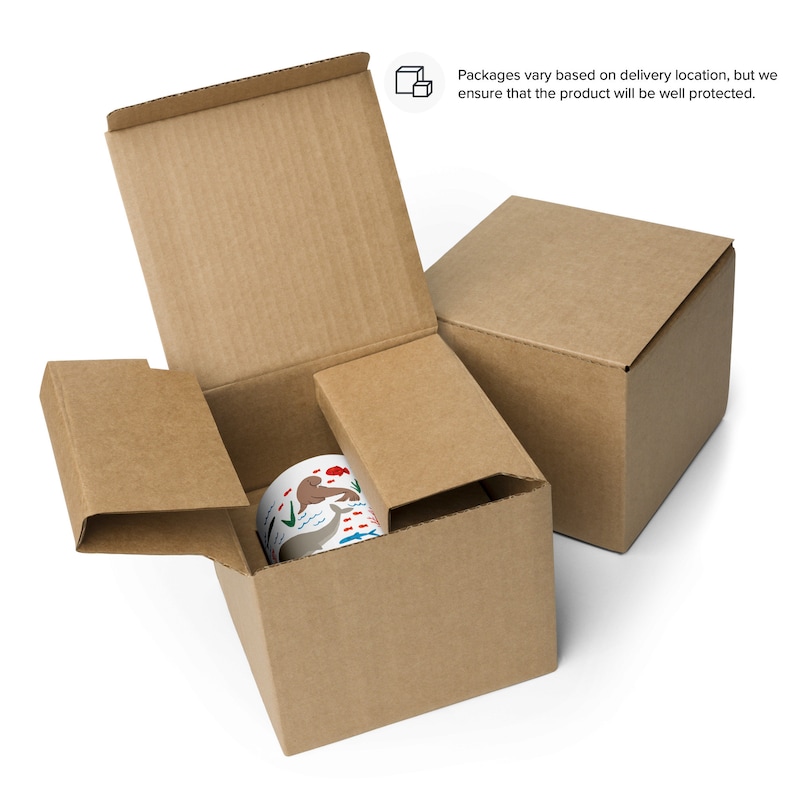 May include: A brown cardboard box with a white mug inside. The mug has a colorful design of animals and plants. The box is open and the mug is visible. The box is sitting on a white surface.