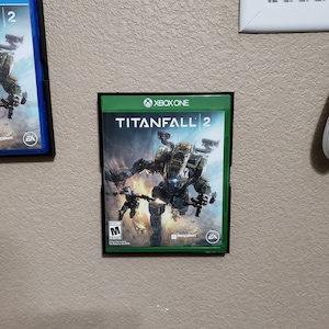 Op de afbeelding: Een videospelcase voor Xbox One met het spel Titanfall 2. De case is zwart met een groene achtergrond en toont een robot en een soldaat in gevecht. De game is geclassificeerd als M voor Mature.