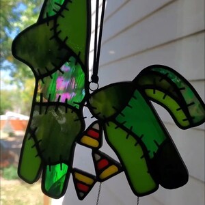 May include: A green stained glass pinata with stitched details and candy corn hanging from it. The pinata is hanging from a black string.