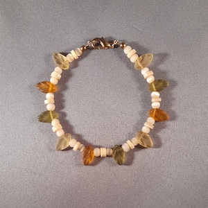 May include: A bracelet with white, amber, and green leaf-shaped beads. The bracelet has a gold clasp.