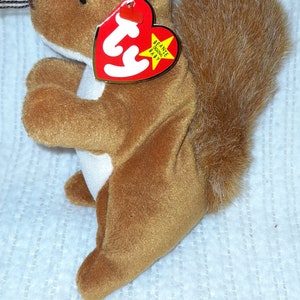 May include: A brown and white plush squirrel with a fluffy tail. The squirrel has a red Ty tag attached to it that says "Beanie Babies".