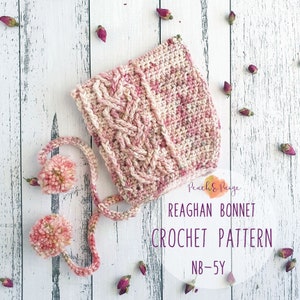 Könnte beinhalten: Eine rosa und weiße gehäkelte Babyhaube mit einem Zopfmuster und zwei Bommeln. Die Haube liegt auf einem weißen Holzgrund mit rosa Rosen. Der Text "Reaghan Bonnet Crochet Pattern NB-5Y" befindet sich auf einem weißen Kreis.
