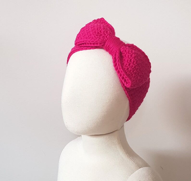 K&ouml;nnte beinhalten: Ein hellrosa geh&auml;keltes Stirnband mit einer gro&szlig;en Schleife. Das Stirnband befindet sich auf einem wei&szlig;en Mannequin-Kopf.