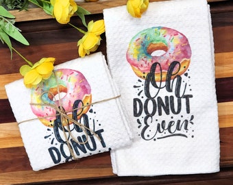 May include: Two white kitchen towels with a colorful donut design and the text "Oh Donut Even" and "Oh Donut Worry" printed on them. The towels are tied together with twine.