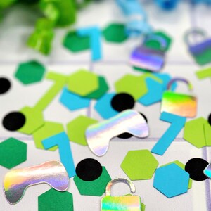 May include: A variety of colorful confetti featuring holographic game controllers, locks, and geometric shapes in green, blue, and black.