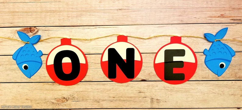 K&ouml;nnte beinhalten: Ein rotes, wei&szlig;es und schwarzes Angler-Schwimmer-Banner, das "ONE" buchstabiert. Das Banner ist mit einer Schnur befestigt und hat an beiden Enden blaue Fisch-Ausschnitte.