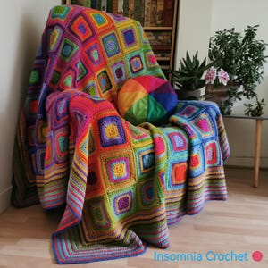 Può includere: Una coperta all'uncinetto colorata con un motivo arcobaleno è drappeggiata su una sedia. La coperta ha un bordo di strisce in vari colori. La coperta è realizzata con filato in tonalità di rosso, arancione, giallo, verde, blu, viola e rosa. La coperta è appoggiata su un pavimento di legno. Il testo "Insomnia Crochet" è visibile nell'angolo in basso a destra dell'immagine.