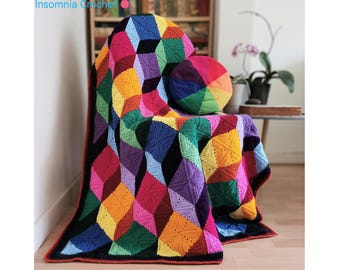 May include: A colourful crocheted blanket with a geometric pattern in shades of red, orange, yellow, green, blue, purple, and black. The blanket is draped over a chair with a matching crocheted cushion.