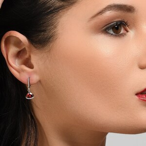 May include: A silver necklace and earrings set with a red heart-shaped gemstone pendant and matching earrings.