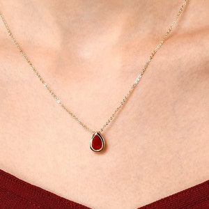 May include: A gold chain necklace with a teardrop-shaped pendant featuring a red gemstone.