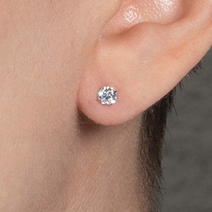 May include: A close-up of a person's ear with a small, round, clear diamond stud earring.