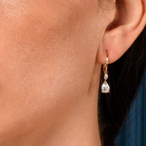 Peut inclure: Gros plan sur le visage d'une femme portant une boucle d'oreille en or avec un diamant en forme de larme qui pend.