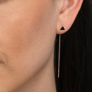 Op de afbeelding: Een vrouw draagt een roségouden ketting en oorbellen. De oorbellen zijn lang en dun met een klein zwart driehoekje aan de bovenkant.