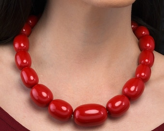 Può includere: Una donna indossa un vestito rosso con una collana di perle rosse. La collana è composta da grandi perle di forma ovale.