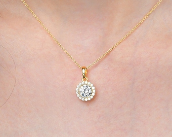 Può includere: Una collana con catena dorata con un ciondolo rotondo che presenta una grande pietra trasparente circondata da pietre trasparenti più piccole.