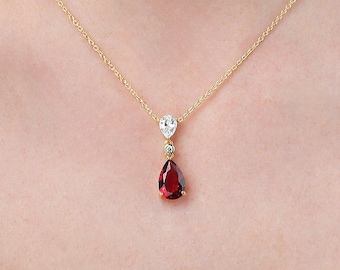 May include: A gold chain necklace with a pear-shaped red gemstone pendant and a smaller clear gemstone above it.