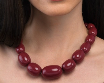 Può includere: Una donna indossa un top color borgogna a spalle scoperte con una collana di perline color borgogna.