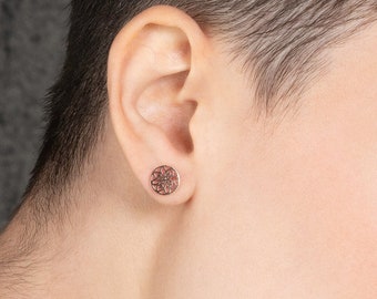 May include: A close-up of a person's face with short brown hair. They are wearing a small, round, rose gold earring in their left ear.