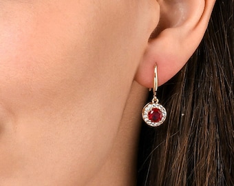 May include: Gold hoop earrings with a red gemstone surrounded by smaller white gemstones.