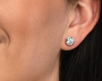 May include: A close-up of a woman's face, smiling with her teeth showing. She is wearing a small, round, clear gemstone earring in her left ear.