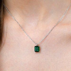 May include: A silver chain necklace with a small, square, emerald green pendant.