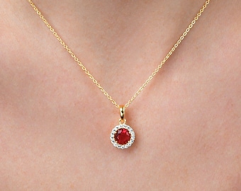 May include: A gold chain necklace with a red gemstone pendant surrounded by a halo of smaller white gemstones.