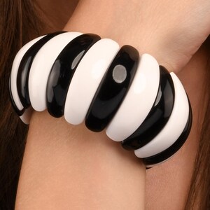 May include: A bold, black and white striped bracelet. The chunky, rounded segments alternate between glossy black and bright white, creating a striking contrast. The bracelet is worn on a wrist, showcasing its design and style.