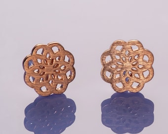 May include: A pair of gold-toned earrings with a delicate, intricate floral design. The earrings are small and round, with a cutout pattern that resembles a flower.
