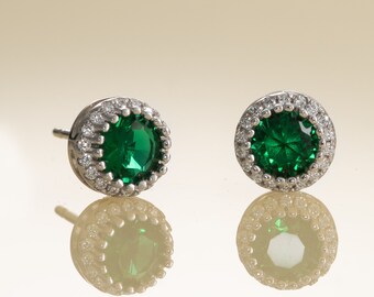 May include: A pair of silver earrings with a green gemstone surrounded by a halo of smaller white gemstones.