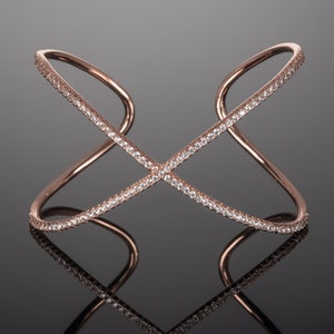 May include: A rose gold cuff bracelet with a criss-cross design, accented with clear sparkling stones.