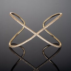 Op de afbeelding: Een gouden armband met een kruisvormig ontwerp en heldere zirkonia-stenen.