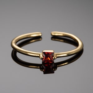 May include: A gold adjustable ring with a small, square, red gemstone.
