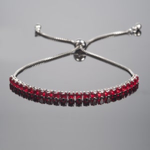 May include: A silver adjustable bracelet with a row of red square-shaped gemstones.