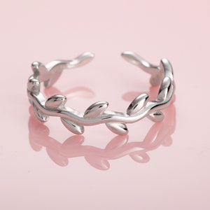 Puede incluir: Un anillo de plata con un delicado diseño de hojas. El anillo es abierto y ajustable para adaptarse a la mayoría de los tamaños de dedos.