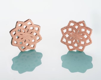 May include: A pair of rose gold earrings with a delicate, intricate mandala design.