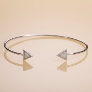 Può includere: Un braccialetto rigido in argento con due accenti triangolari di opale. Il braccialetto è aperto e ha un design semplice.