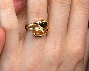 Op de afbeelding: Een gouden ring met een zwarte steen. De ring wordt gedragen op de middelvinger van een hand met gemanicuurde nagels.